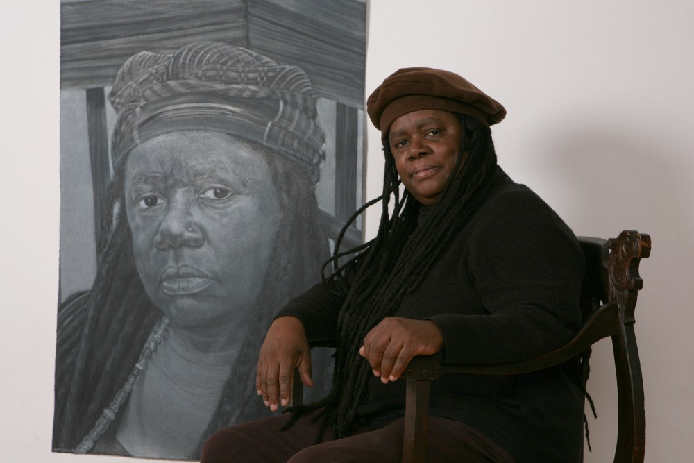 Diane Edison seated in front of her 2010 Self-Portrait drawing