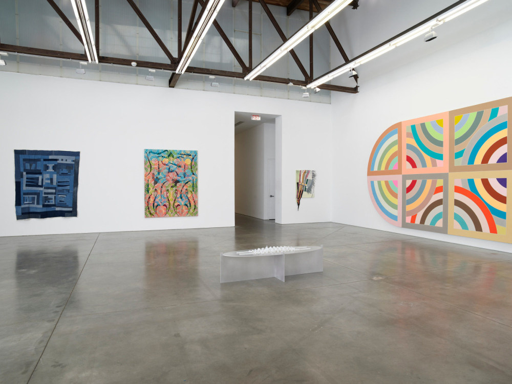 4 abstract, patterned paintings and textile pieces hung in a large art gallery