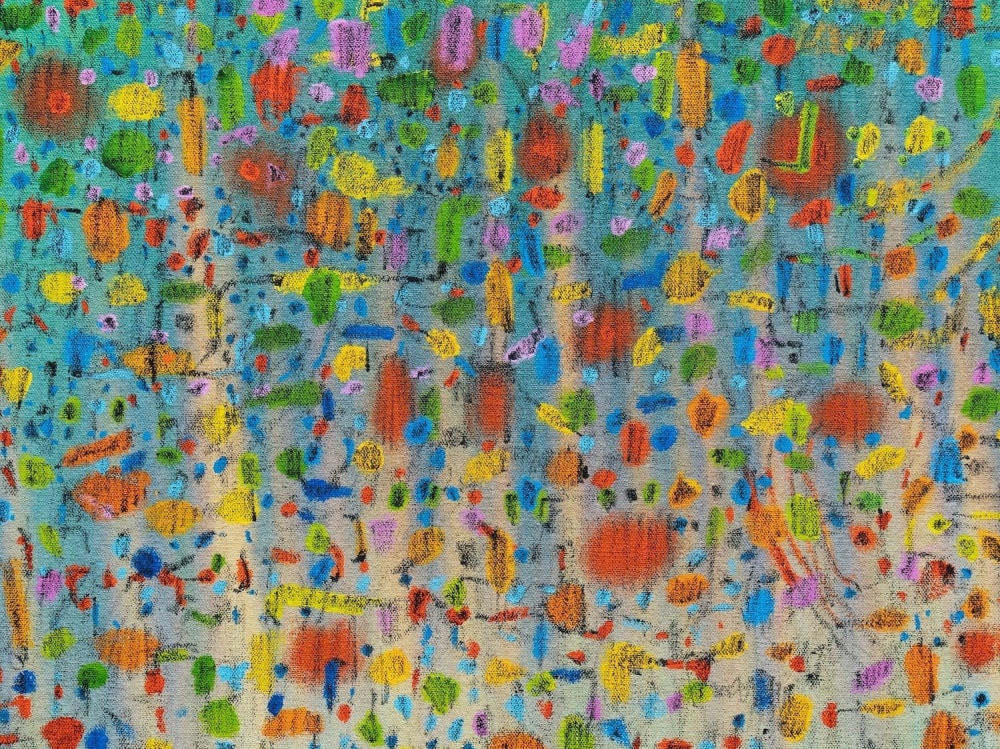 Close up of abstract painting with multiple marks and shapes in red, yellow, green and orange over a blue to cream background