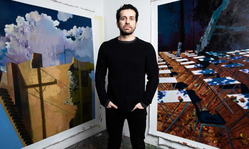 Man standing between 2 paintings of landscapes and buildings