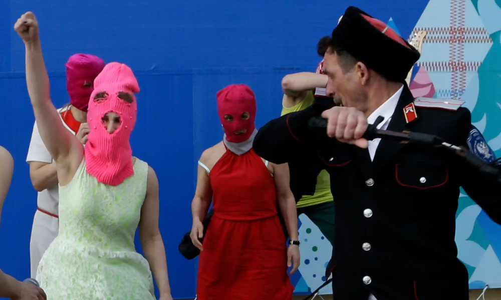 A performance by the band Pussy Riot: 3 women in stocking caps and a man dressed as a policeman