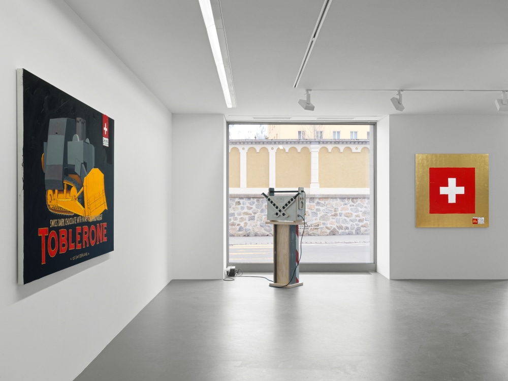 Installation shot of Tom Sachs' exhibition in St. Moritz, showing a Toblerone painting, a swiss flag painted on gold leaf and a boombox on a socle