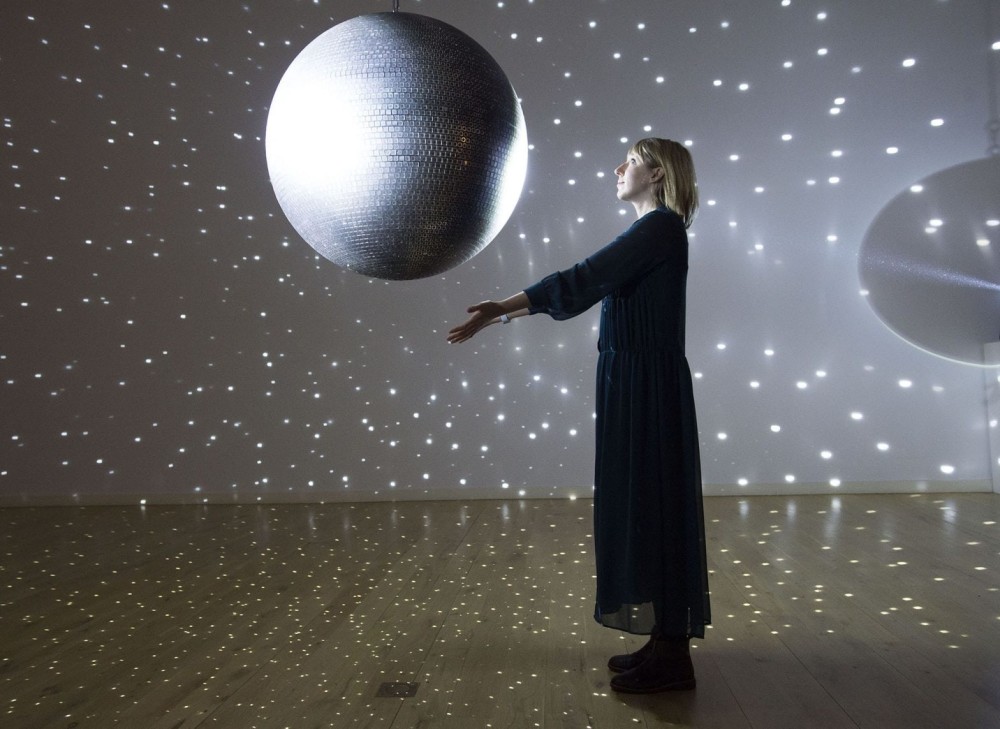 Katie Paterson looking at a mirror ball which is actively reflecting specs of light across the room
