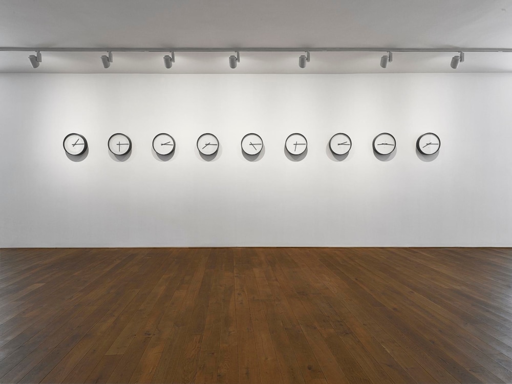 nine clocks placed next to each other in a horizontal manner, hanging on a plain white wall