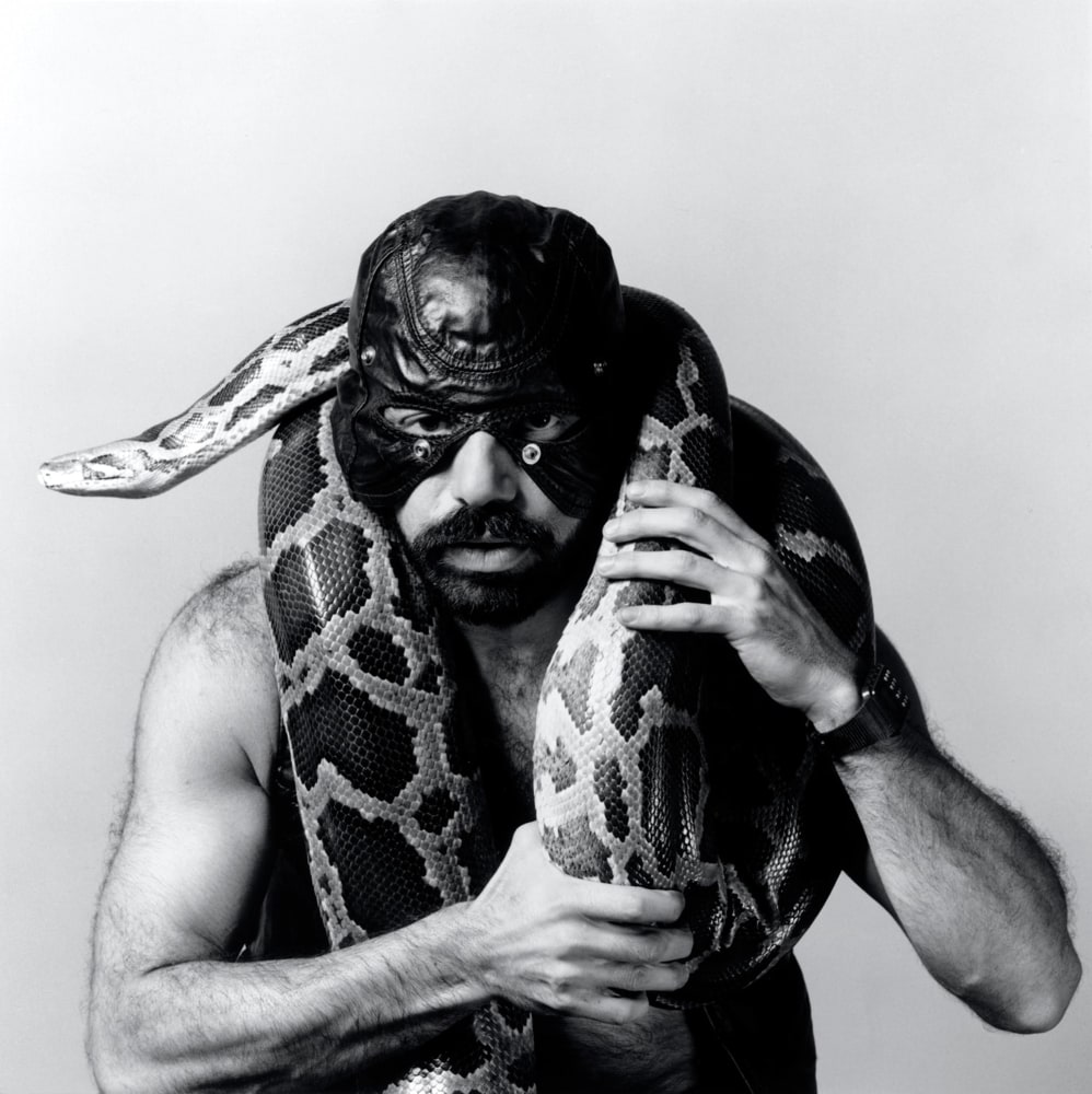 Man wearing leather mask, holding snake around neck.