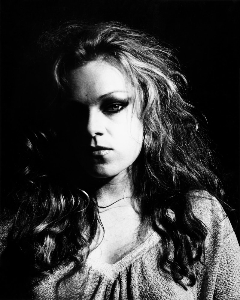 High contrast portrait of Cookie Mueller, with half her face in shadow.