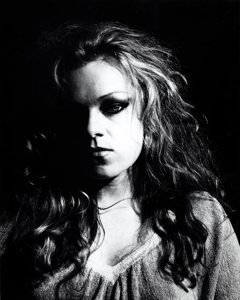High contrast portrait of Cookie Mueller, with half her face in shadow.