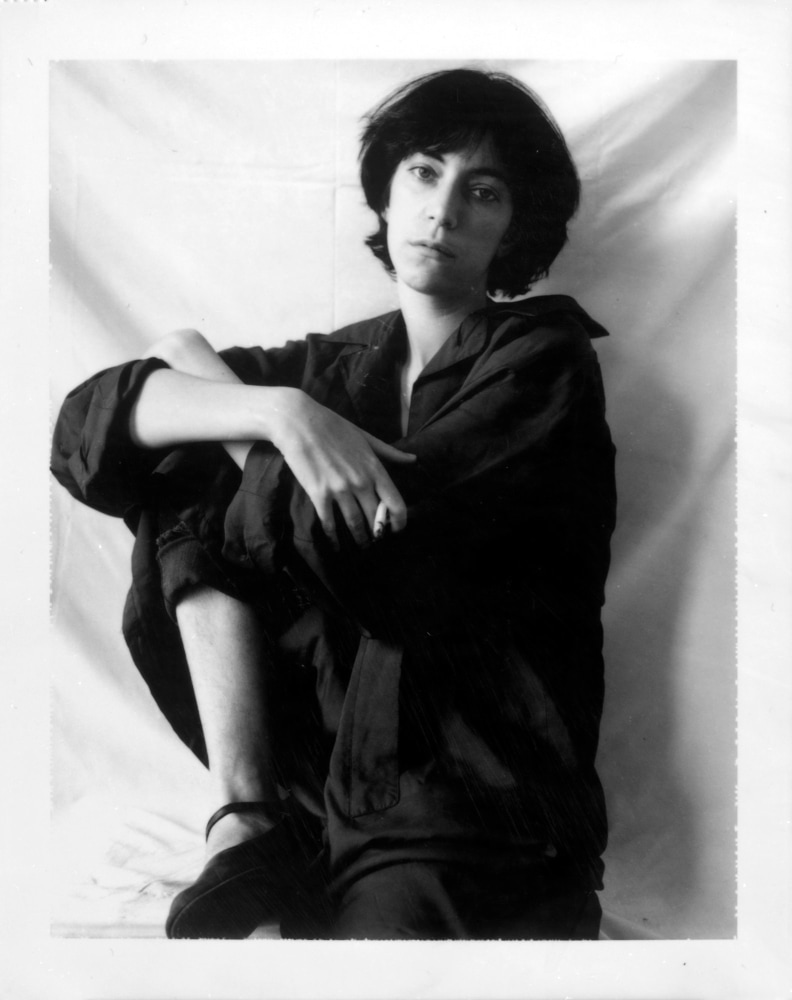 Polaroid image of Patti Smith sitting on a stool with arms wrapped around one knee.
