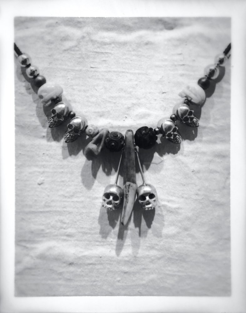 Polaroid image of Robert's jewelry--a beaded necklace with two dangling skulls.