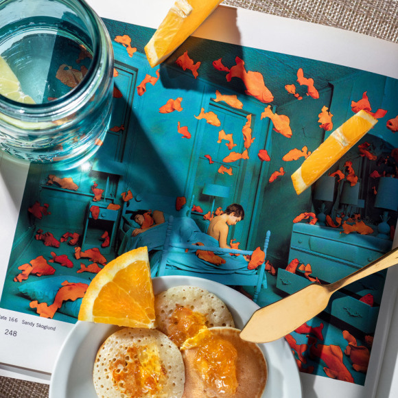 Sandy Skoglund staged  photo of a blue room with gold fish appearing to swim though the air, rephotgrpahed with breakfast foods on top.