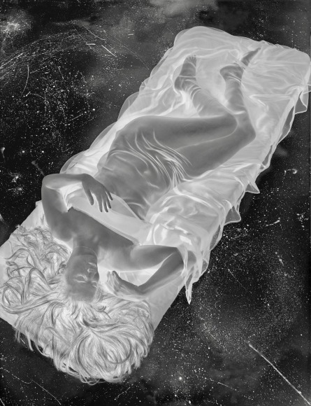 Negative image of woman, nude except for a transparent sheet, reclining on a mattress.