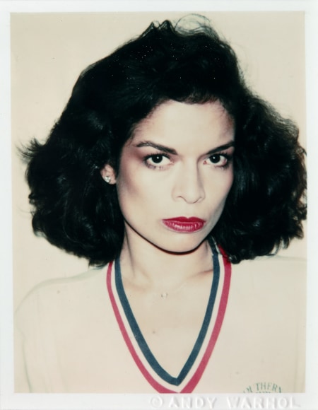 Polaroid portrait of a young Bianca Jagger wearing a sweater with blue and red trim at the neck.