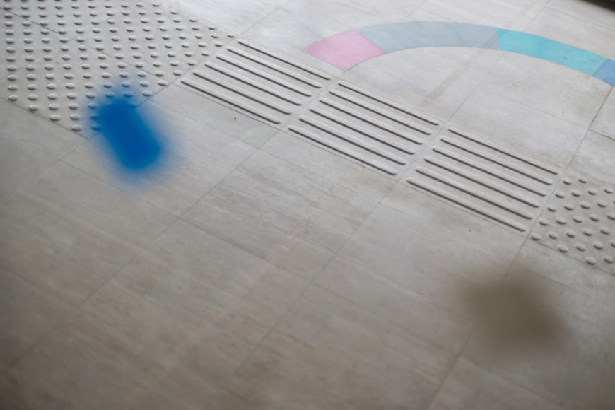 Color photograph showing an abstract composition created with a concrete shape on the ground, and a blue out of focus object in the foreground.