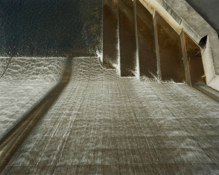 Color photo of a view from above looking down at water pouring down a spillway.
