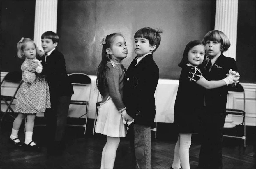 Black and white image of six young children coupled up to take dance lessons, looking at the instructor off camera.
