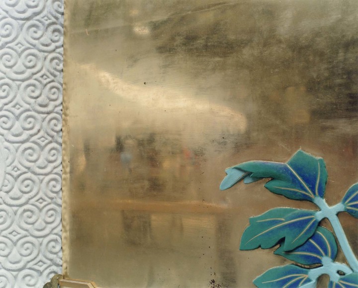 Close up color photo of a gold wall with a sculpted plant decoration on the right.