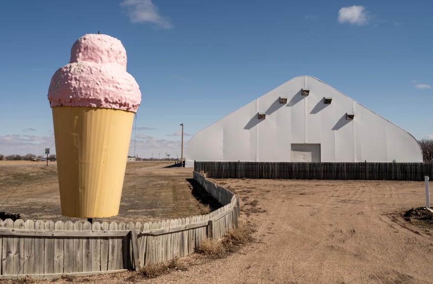 Color photo of a large ice cream cone statue in a rural area next to a barn.