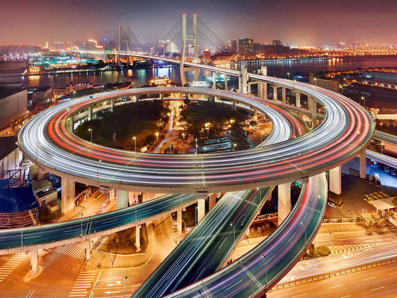 Long exposure photograph of cars driving on the spiral ramp of a Shanghai bridge.