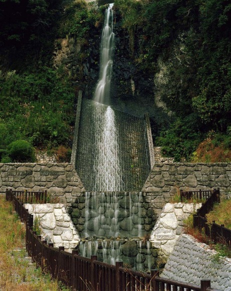 Water falling down an engineered embankment in a wooded area.