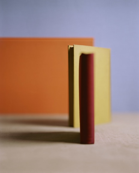Sahllow focus photograph of three differently colored books standing on end in from to a blue background, two are out of focus.