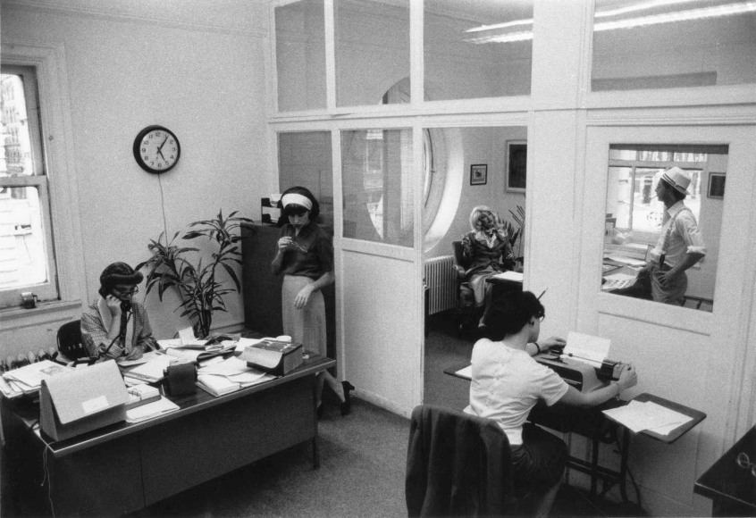 black and white photo of office and office workers, dressed in a mid-century style.
