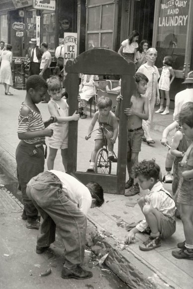 Black and white photo of a group sod you young boys paling with the frame that previous held a mirror, now broken. A boy on a tricycle is framed in the broken mirror.
