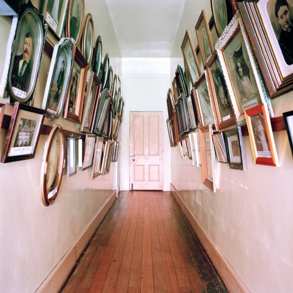 Color photo of a hallway hung with many framed images, leading to a door at the end of the hall