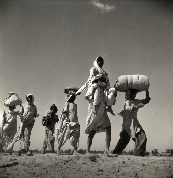 Low angled black and white photo of refugees walking across a desert landscape.