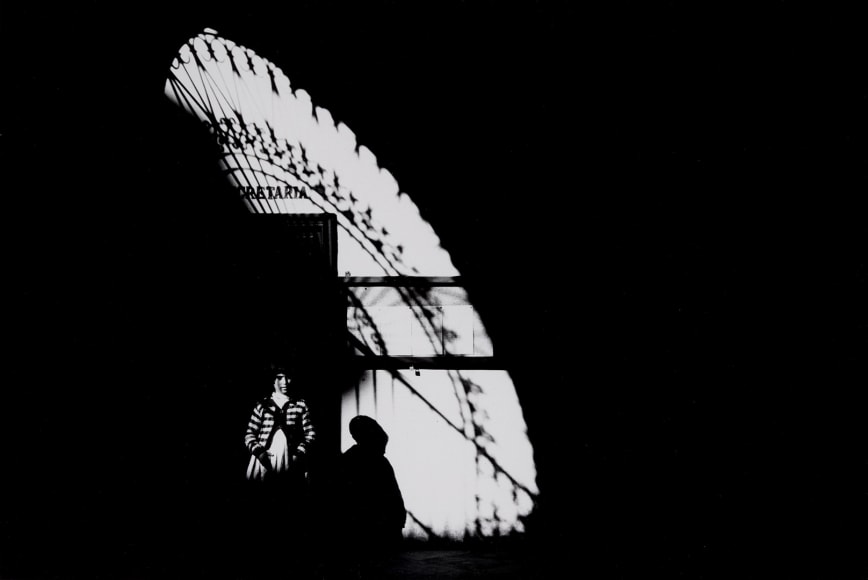 Black and white photograph by Ray Metzker showing a child in light and sad from a grilled doorway in Spain&mdash;shot in 1960