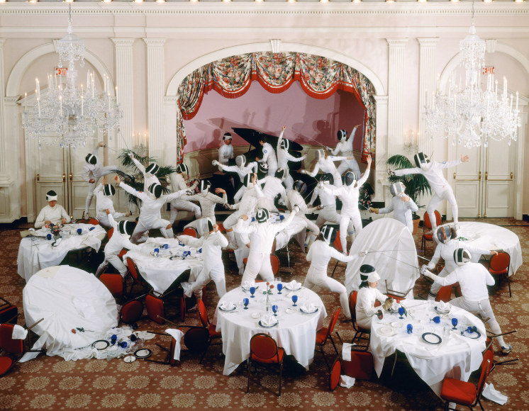 Color photograph of a staged fight by a group of fencers in a ballroom&mdash;tables that are served for dinner have been knocked over  by the fencers.