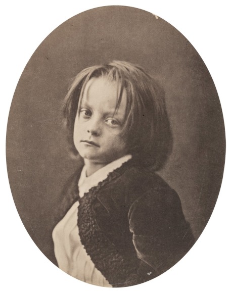 Oval vintage black and white portrait of young boy with longish hair.