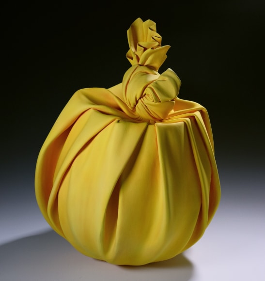 Tall yellow sculpture in the shape of furoshiki (wrapping cloth) containing rounded vessel with large knot, 2022