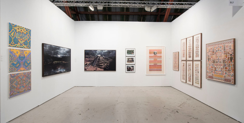 Installation of art fair booth, showcasing paintings, collages, and photos on the walls.