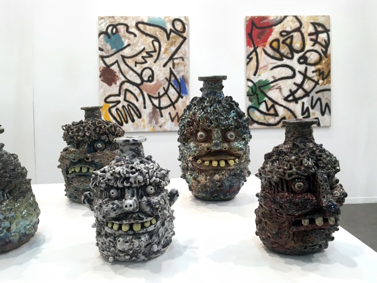 Installation view of the art fair booth at Zona Maco. Paintings are on the walls behind sculptures on a table