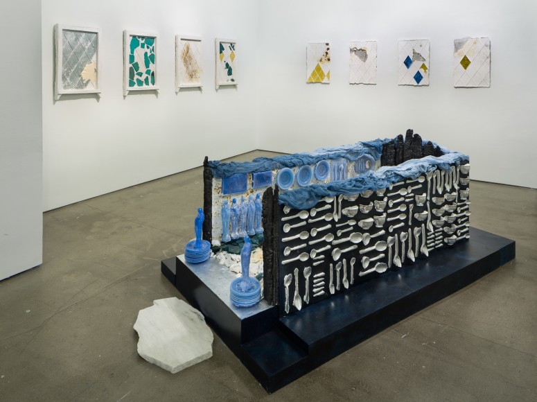 Mixed media pieces line the walls and a large rectangular installation is on the floor.