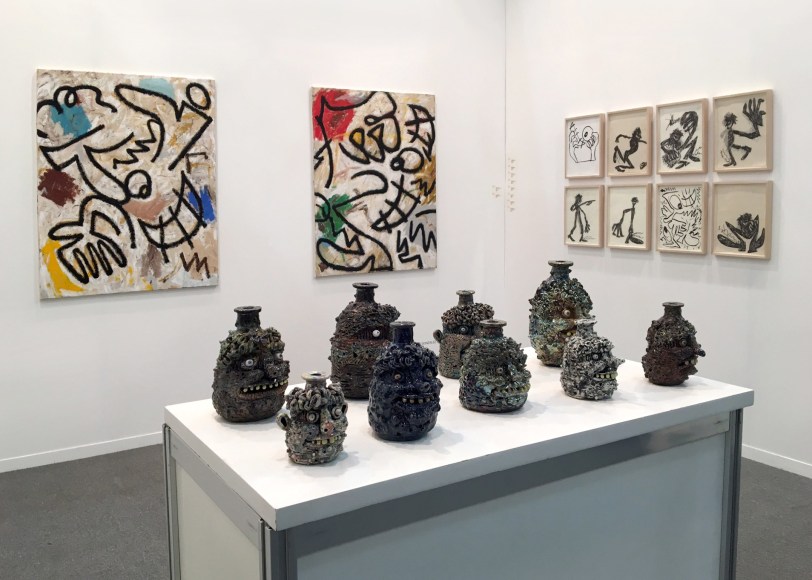 Installation view of the art fair booth at Zona Maco. Paintings are on the walls and sculptures are on a table