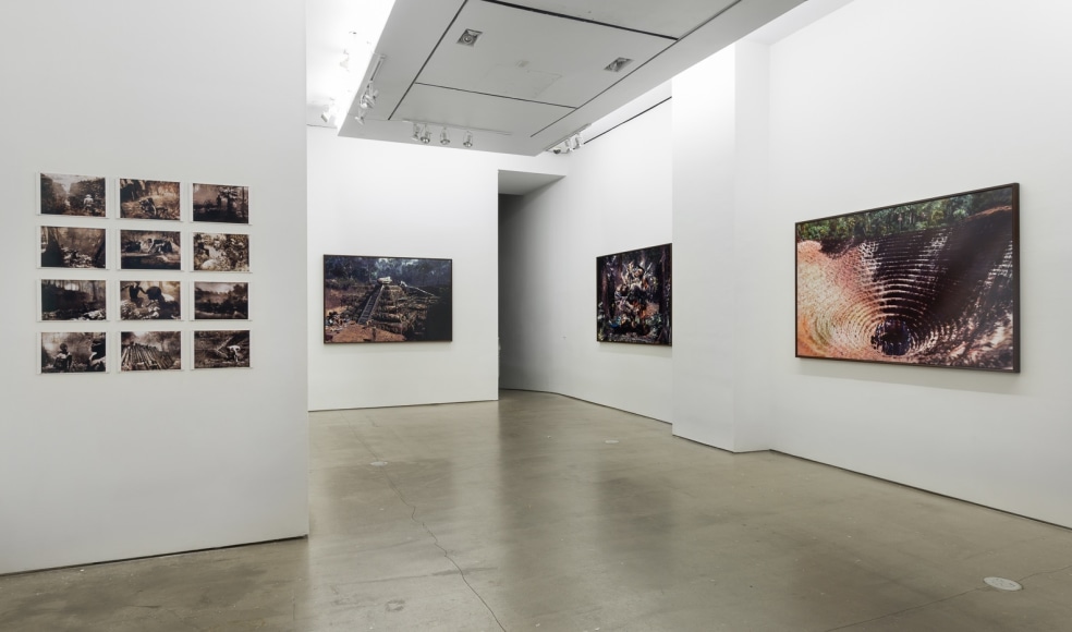 An installation view of Jasper de Beijer's exhibition, "The Brazilian Suitcase". Framed photographs are on the walls. Small pieces are arranged in a grid.