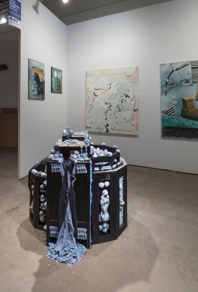Installation view of an open art fair booth, showcasing artwork on the walls. A large &quot;wishing well&quot; installation is on the floor.
