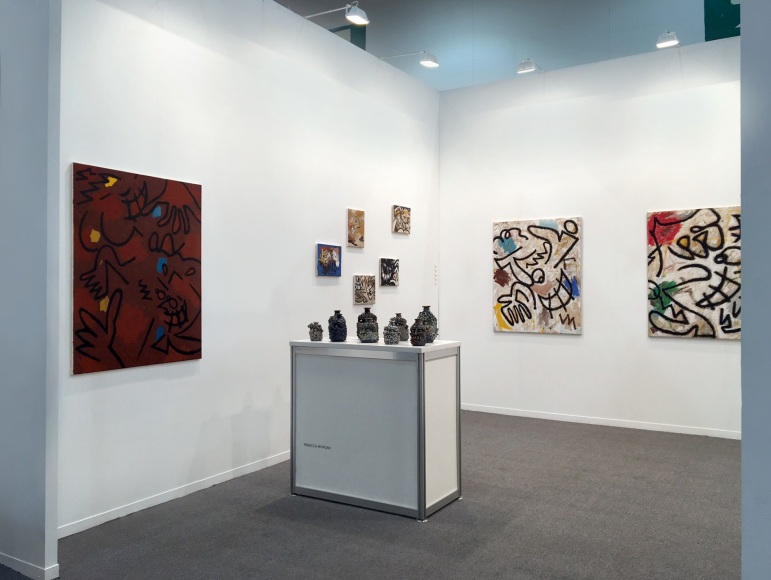 Installation view of the art fair booth at Zona Maco. Paintings are on the walls and sculptures are on a table