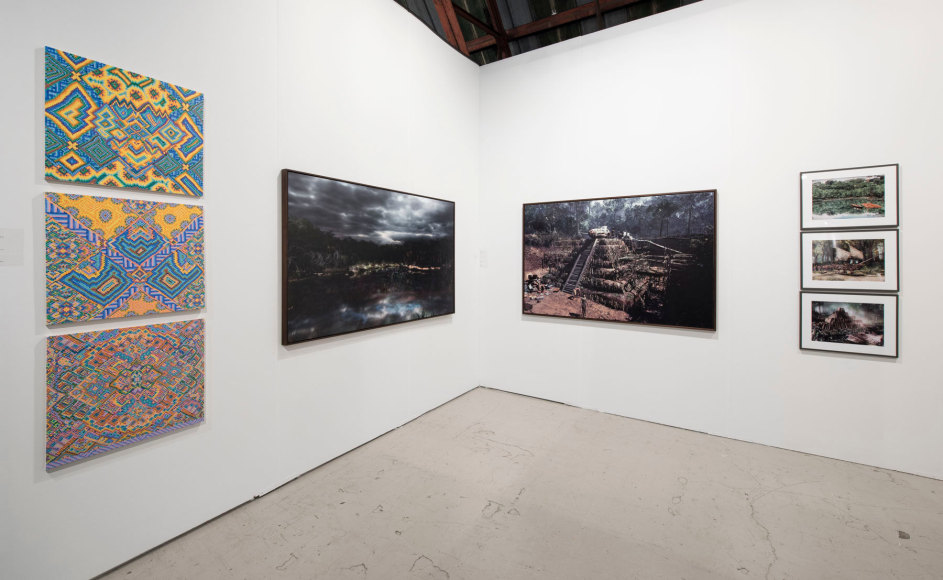 Installation view of an art fair booth, showcasing paintings, collages, and photos on the walls.