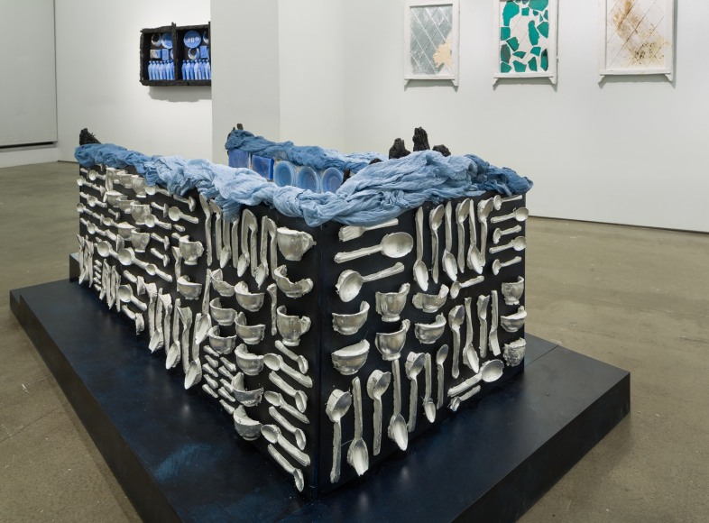 An installation of artwork by Julie Schenkelberg. Mixed media pieces line the walls and a large rectangular installation is on the floor.