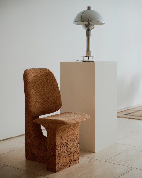 Installation view of works in the gallery, mostly furniture and some rugs and art. Cork chair next to lamp.