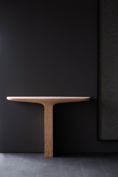 Cork console table with one leg by Noe Duchafour-Lawrance. Photographed against a dark grey wall.