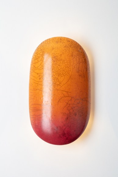 Raku glaze orange and red crackle effect on a pill shaped wall sconce. light turned on in image.