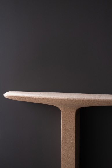 Cork console table with one leg by Noe Duchafour-Lawrance. Photographed against a dark grey wall.