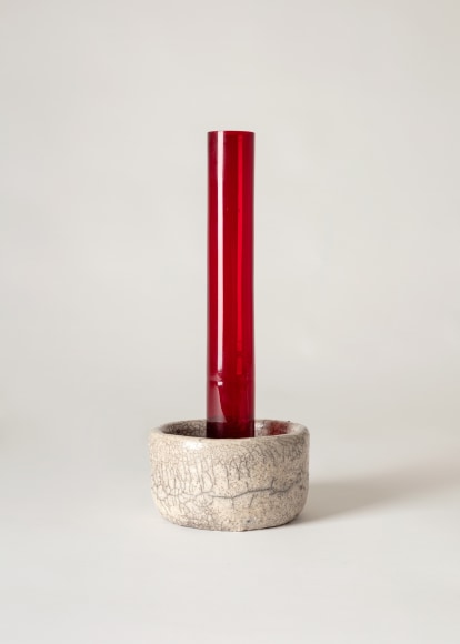 Red glass tubular vase sitting inside raku ceramic holder.