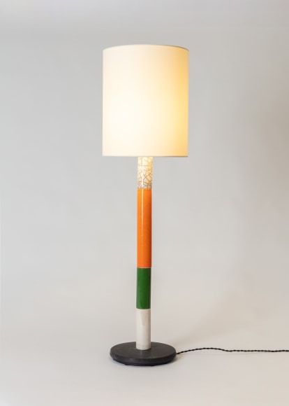 Floor lamp in various colors, white fabric shade. Colors from bottom to top, black base, white section, green section, orange, white raku. Light is illuminated