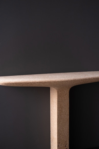 Cork console table with one leg by Noe Duchafour-Lawrance. Photographed against a dark grey wall.