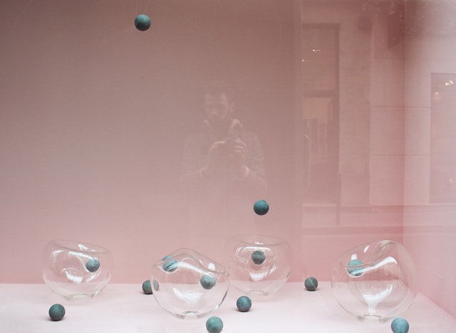 photograph of a display case with pink wallpaper containing amorphous glass spheres and concrete balls