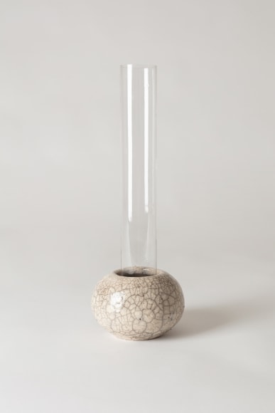 Clear glass tall tubular vase sitting inside raku ceramic holder.